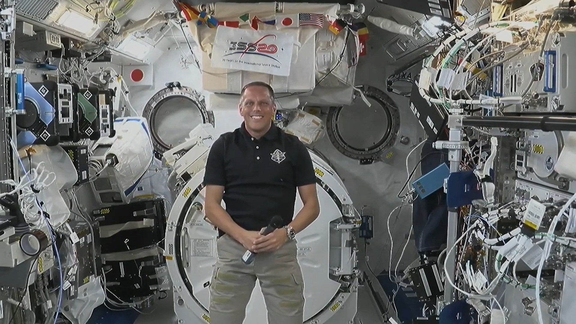 A man floating in a space station looking at the camera.