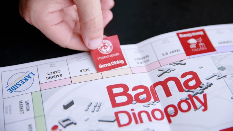 someone places a stick on a game board for Bama Dine-opoly