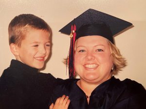 A small boy next to a woman wearing graduation regalia. 