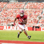 a Crimson Tide football player running with the ball on the field