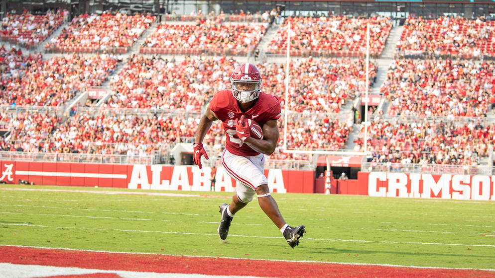a Crimson Tide football player running with the ball on the field