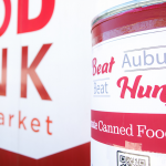 A red collection barrel for nonperishable food items sits in front of a West Alabama Food Bank trailor.