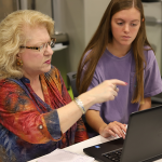 A student helps an adult at a computer.