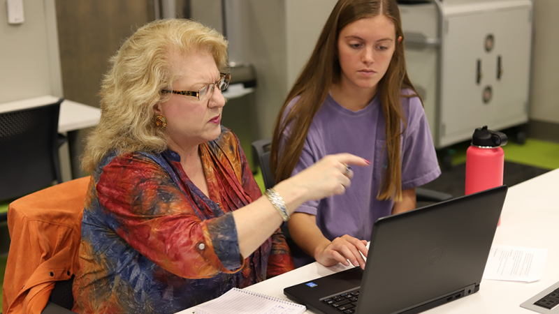 A student helps an adult at a computer.