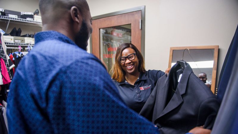 a young woman shows a sport coat to a male student inside the crimson career closet
