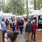 a crowd of people walk amongst tents at the art festival