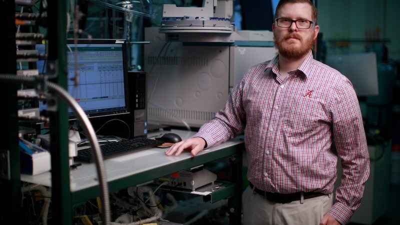 A man in red-checked dress shirt poses for a photo in a lab.