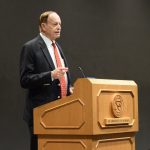 A man in a suit speaks from a podium.