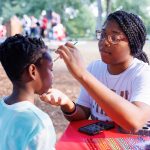a young child has his face painted by a volunteer