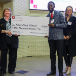 A winner is presented a large check for $1,000 at a River Pitch Competition.