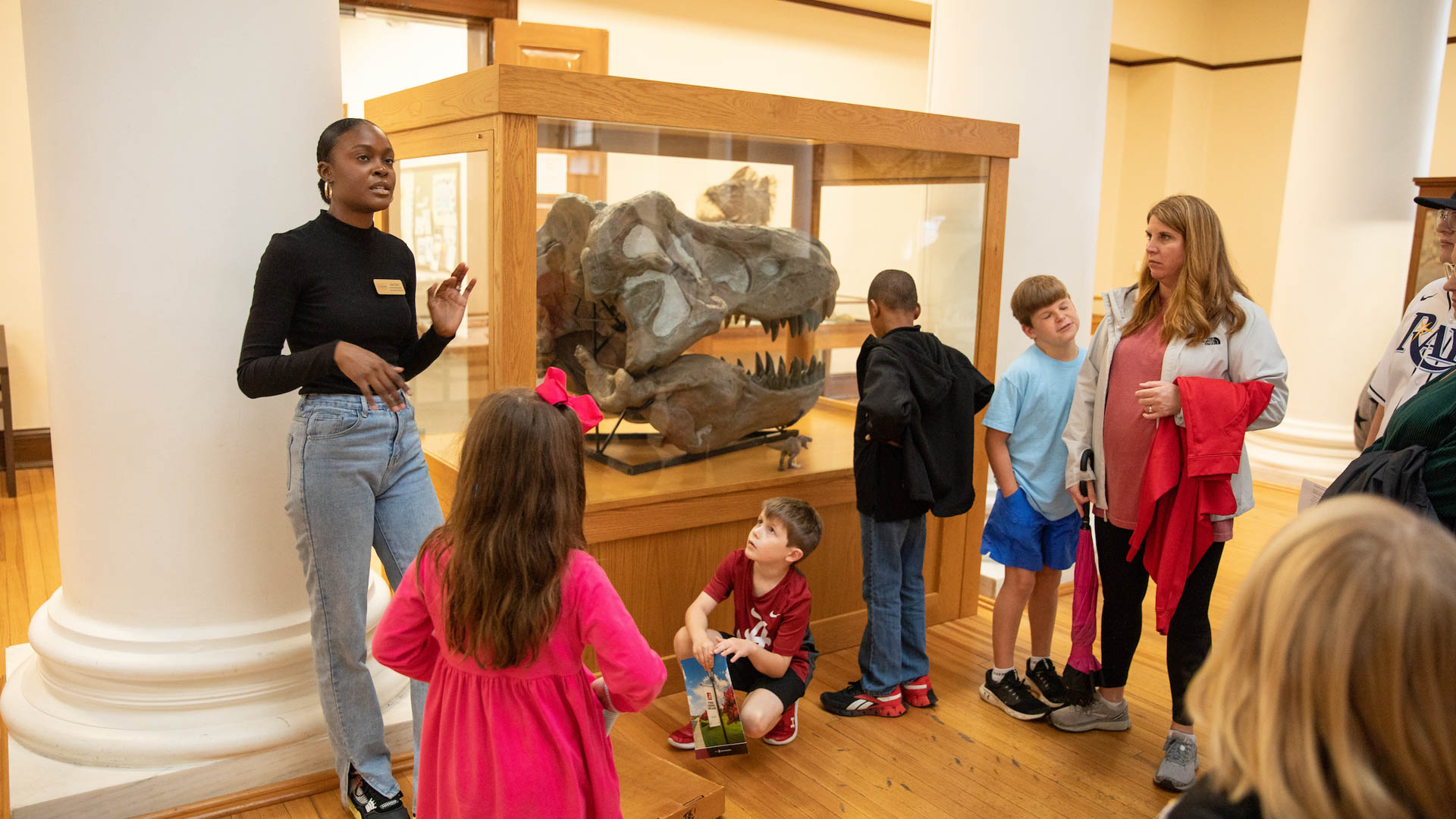 children and parents stand neat a dinosaur fossil on a tour of the Alabama Museum of Natural History