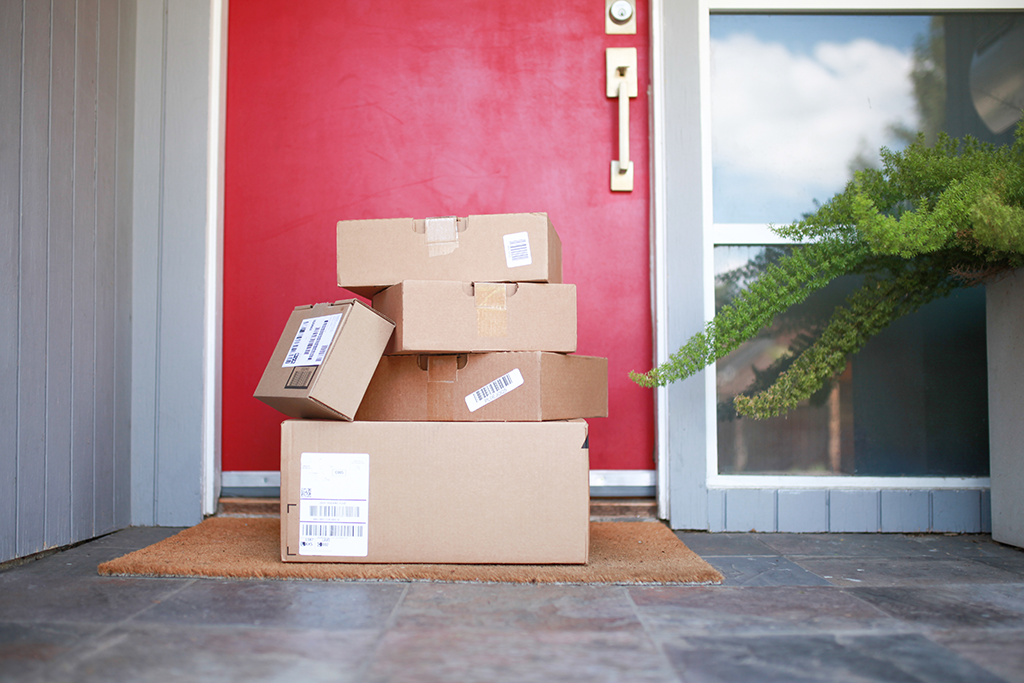 Packages stacked on a porch in front of a red door.