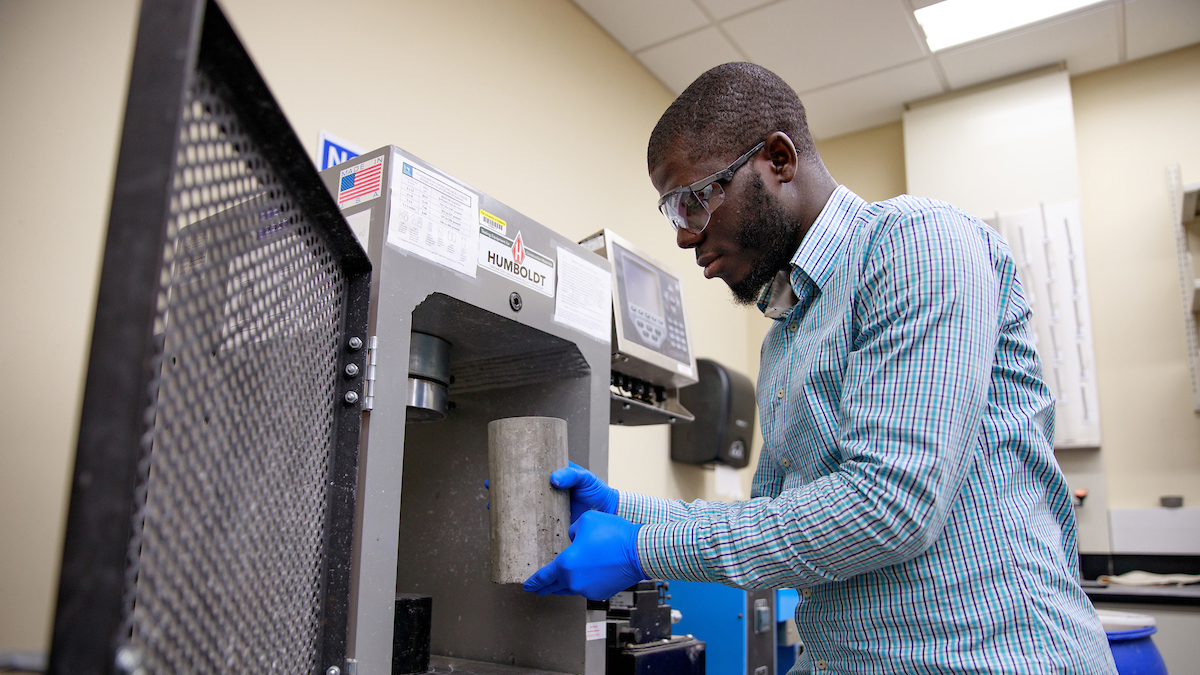 An engineering graduate student at The University of Alabama places cylindrical samples of concrete into a machine.