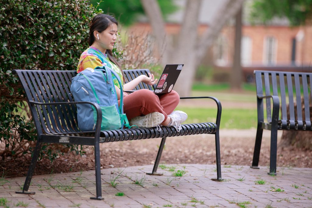 Woman looks at laptop while sitting on Quad bench