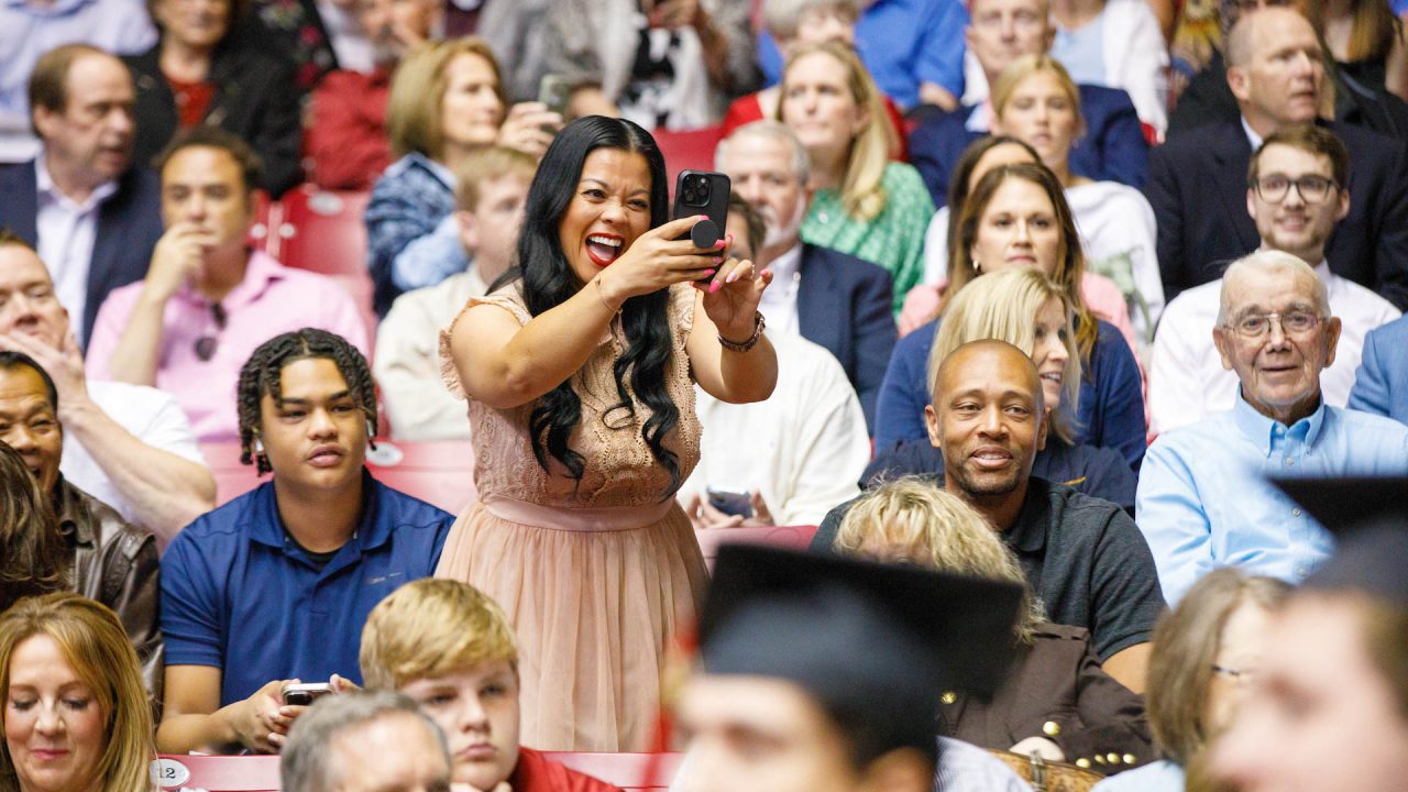 a woman stands up in her seat smiling while taking a picture with her phone