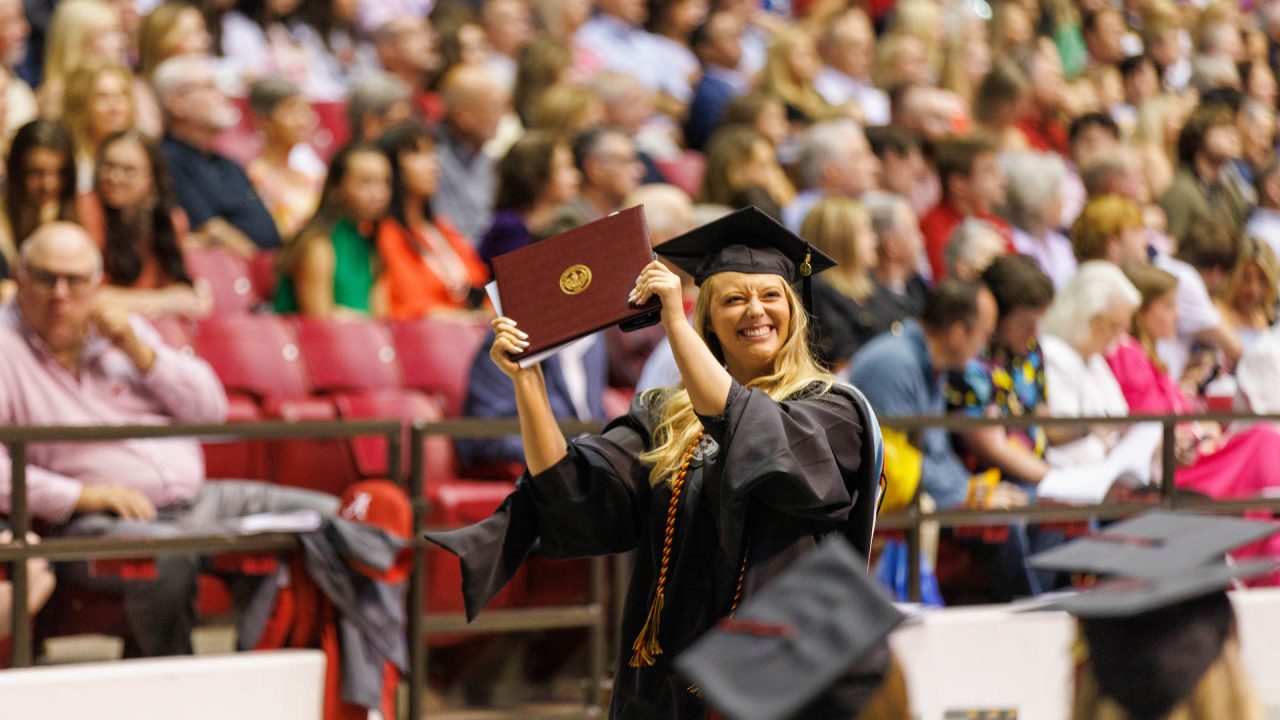 a young woman holds up her diploma triumphantly