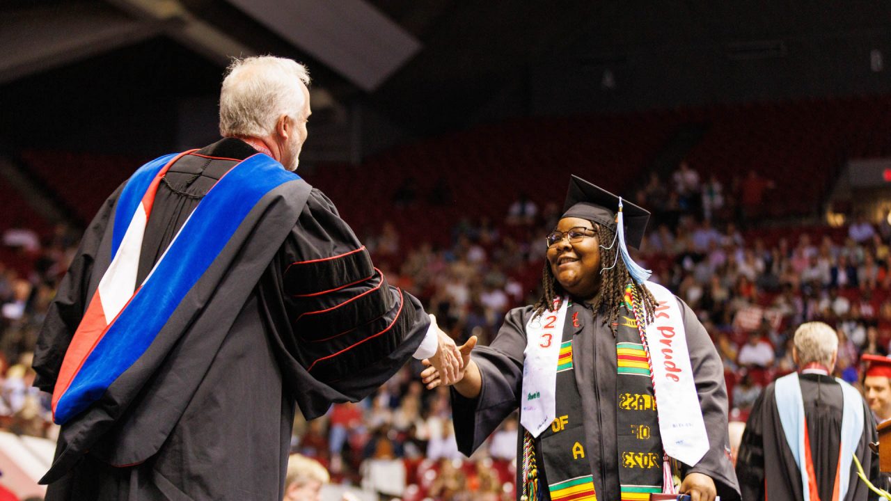 a young woman shakes Dr. Bell's hand on the commencemennt stage