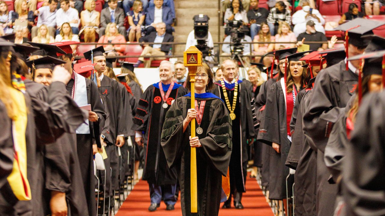 a faculty member carries the ceremonial mace during commencement