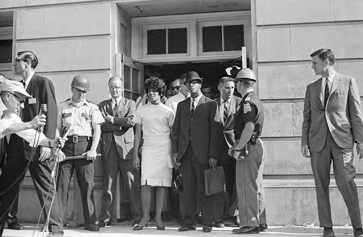 An historical photo two African American students surrounded by law enforcement, officials and media as they register for classes at The University of Alabama.