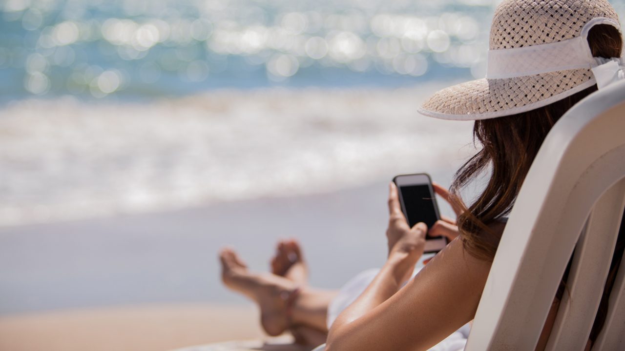 a woman sits in a chair on the beach looking at her phone