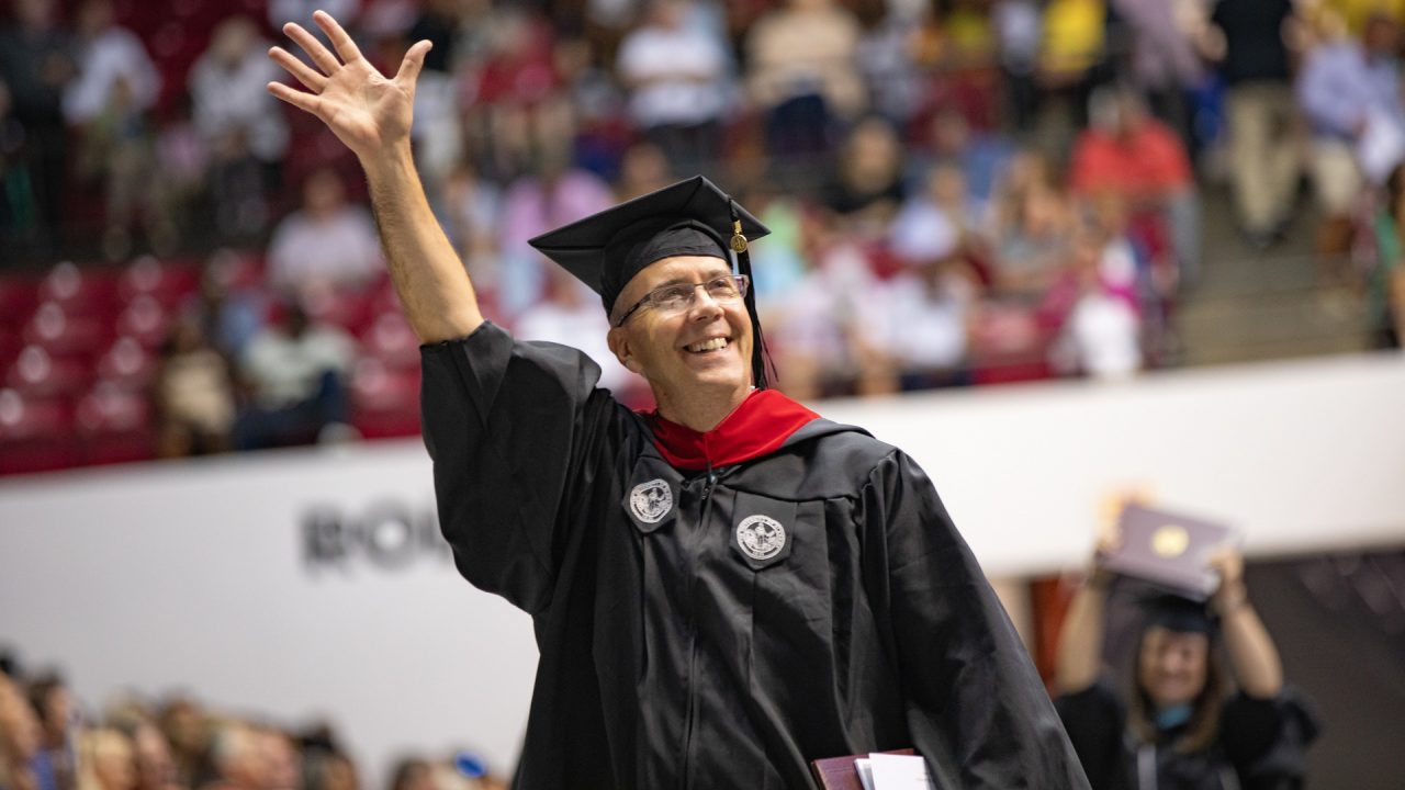 a graduate waves after walking across the stage
