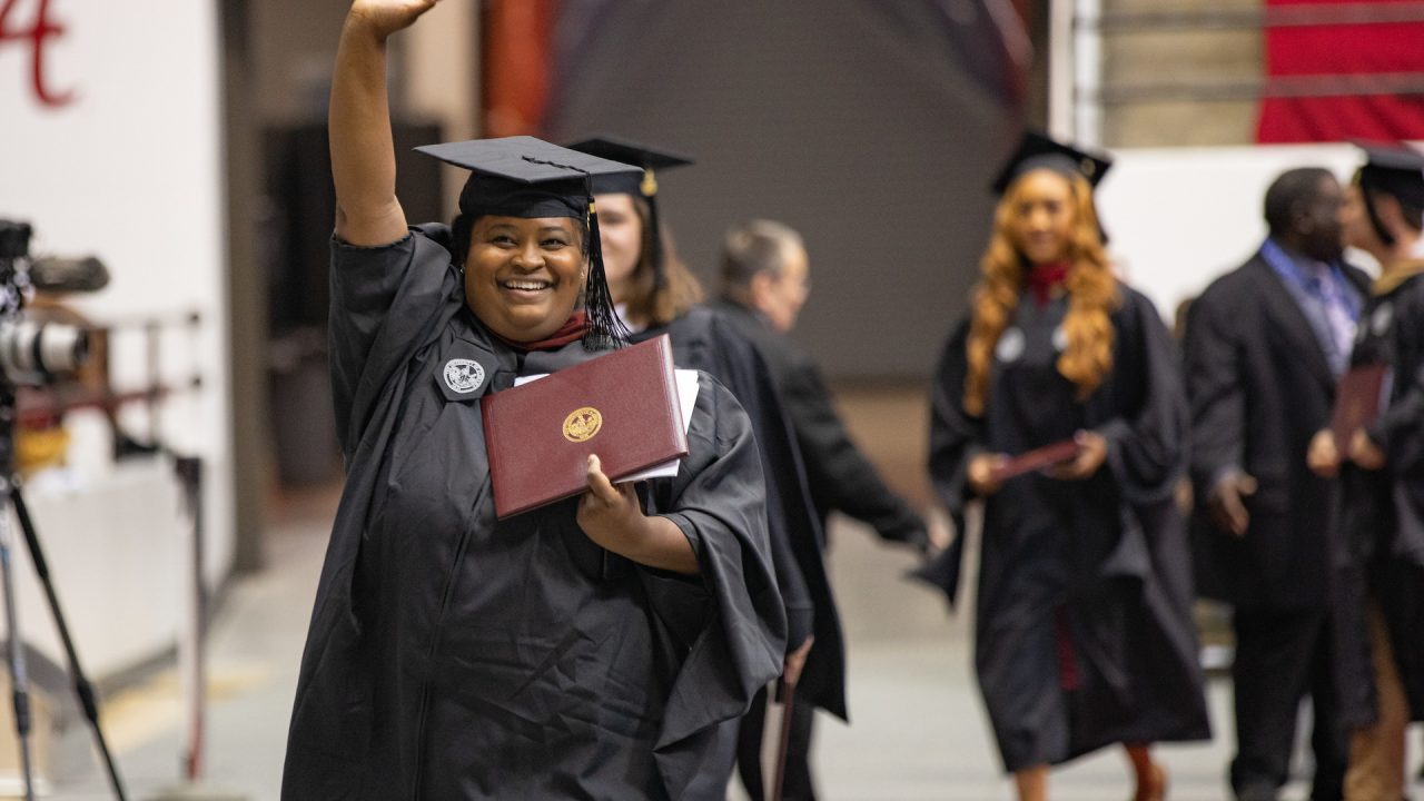 a student waves while holding her degree