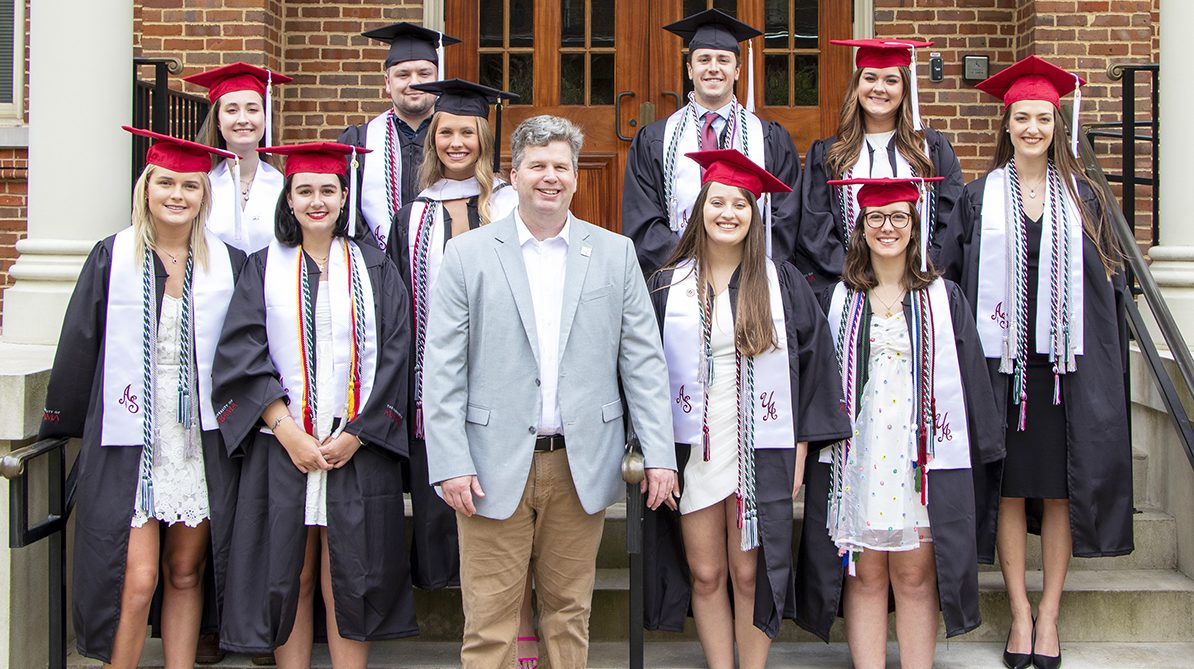 A group of pre-medical students wearing graduation attire stand with a professor.