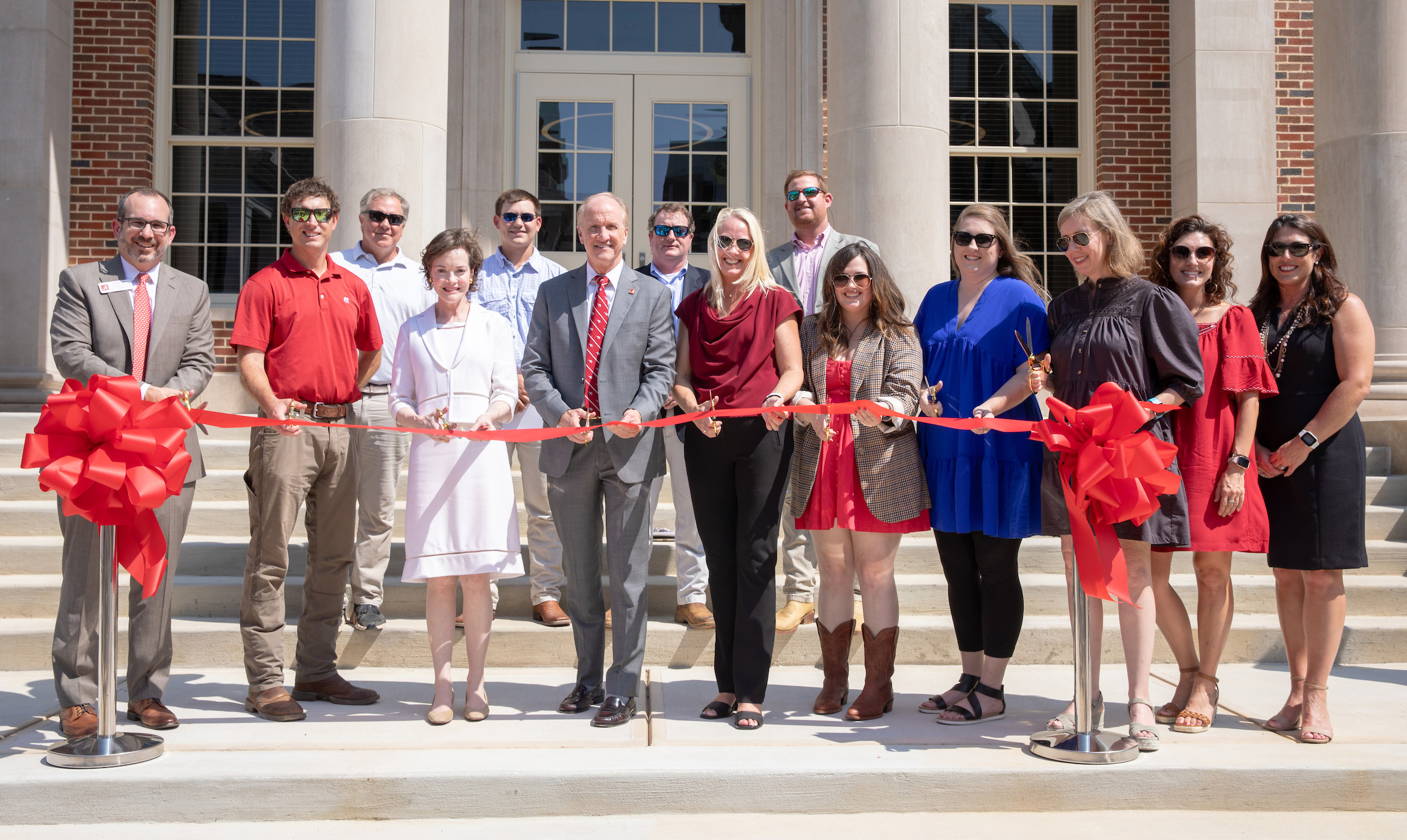 group of people hold a red ribbon for a ribbon cutting
