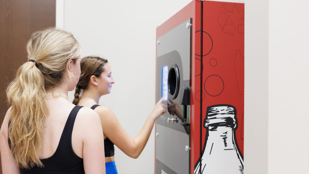 Two girls use a reverse vending machine to recycle a bottle.