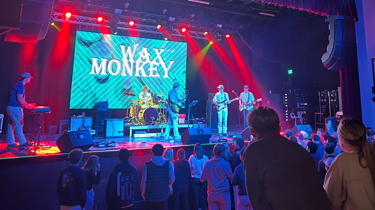 UA student band Wax Monkey performs on a stage under concert lights.