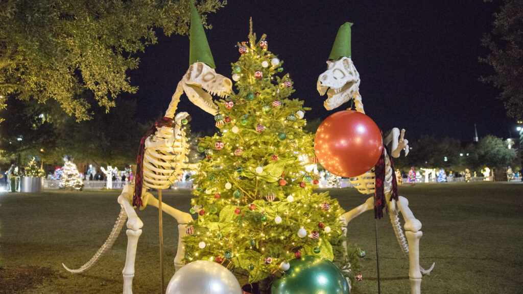 a Christmas tree flanked by two T-Rex skeleton's wearing elf hats for Tinsel Trail December event