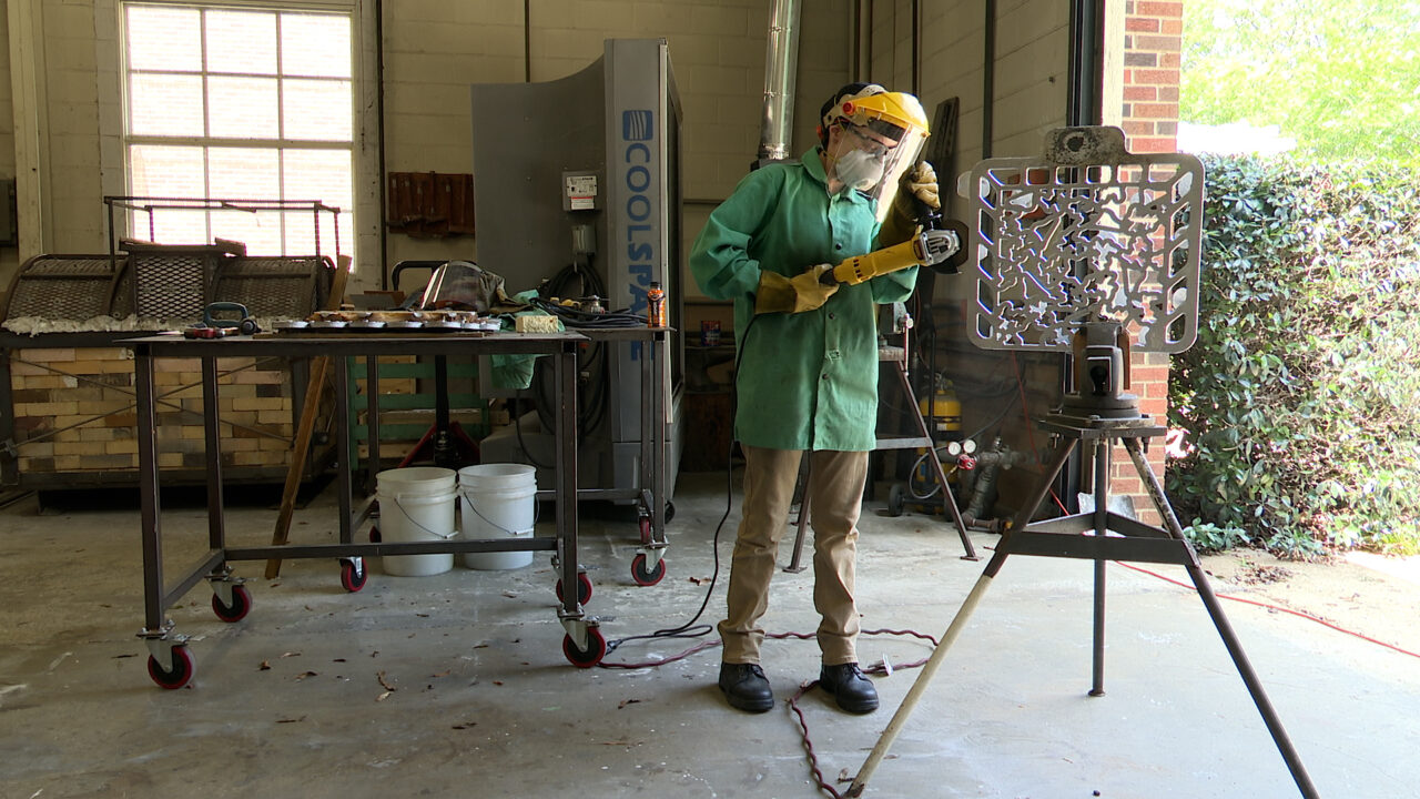a student welder wearing a mask while working on a piece of cast metal art