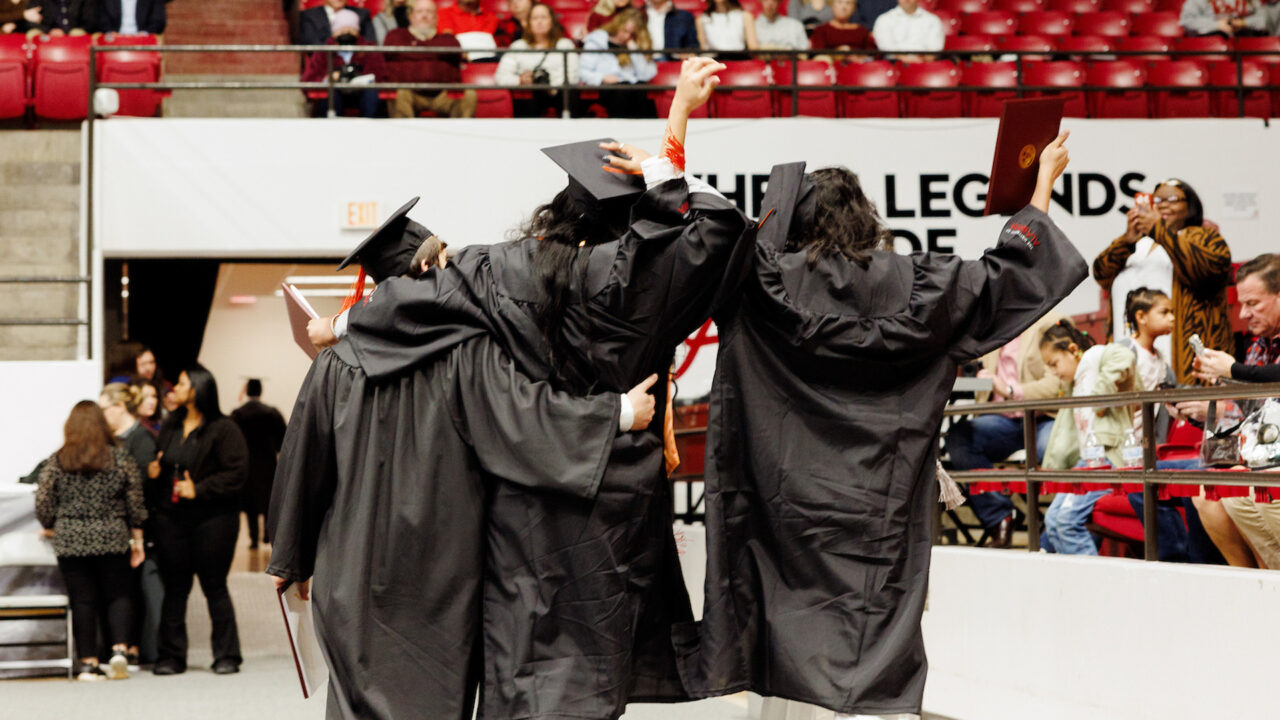 three graduates leave the stage with their arms draped over each other's necks