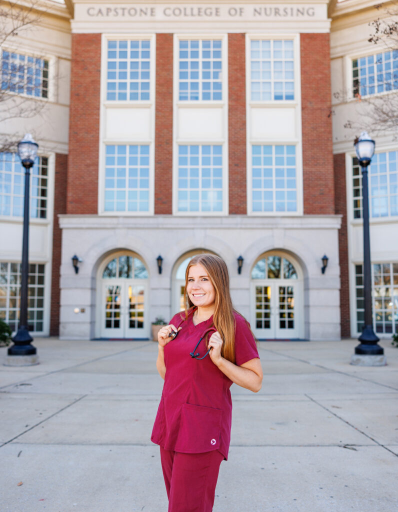 Megan Butterworth wearing crimson scrubs standing in front of the Capstone College of Nursing