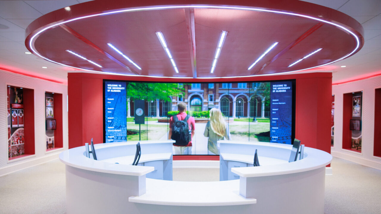 The entrance to the Randall Welcome Center with a reception desk and a dynamic, floor-to-ceiling screen displaying imagery from the University and current visitor's names.