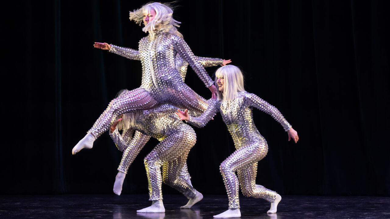 a group of dancers dressed in shiny metallic costumes on stage