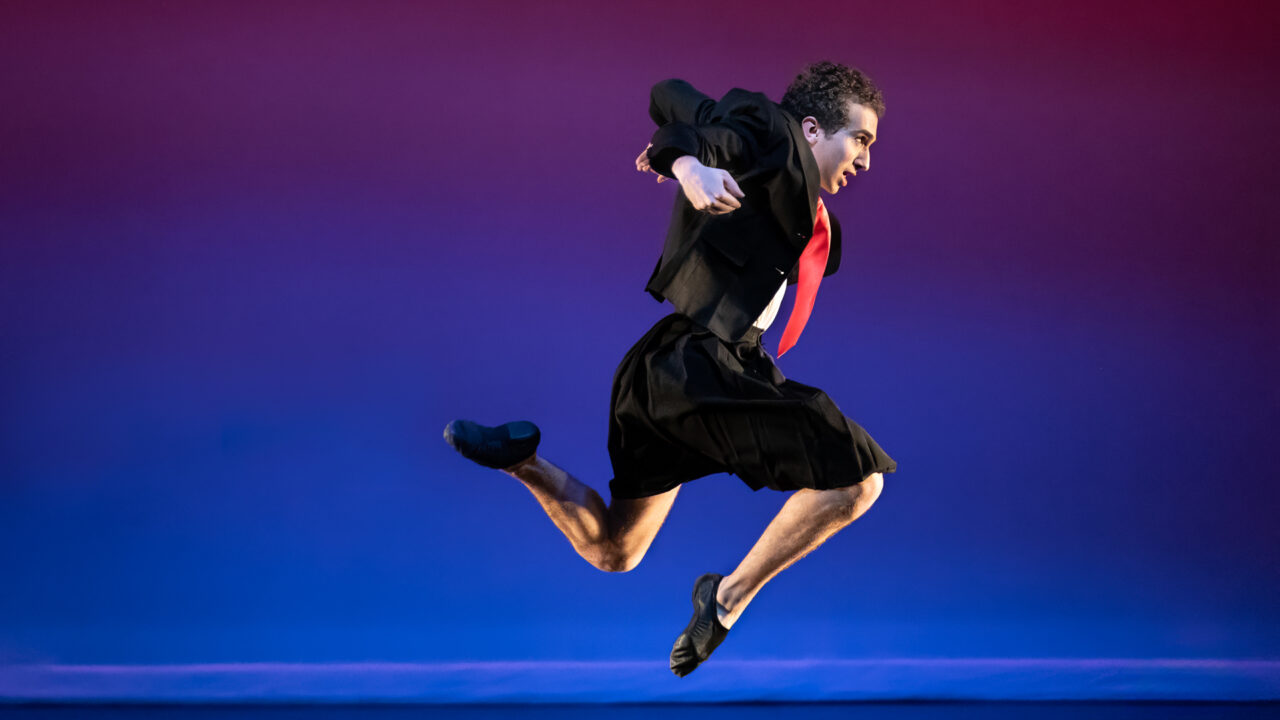 a male dancer jumps in the air on stage