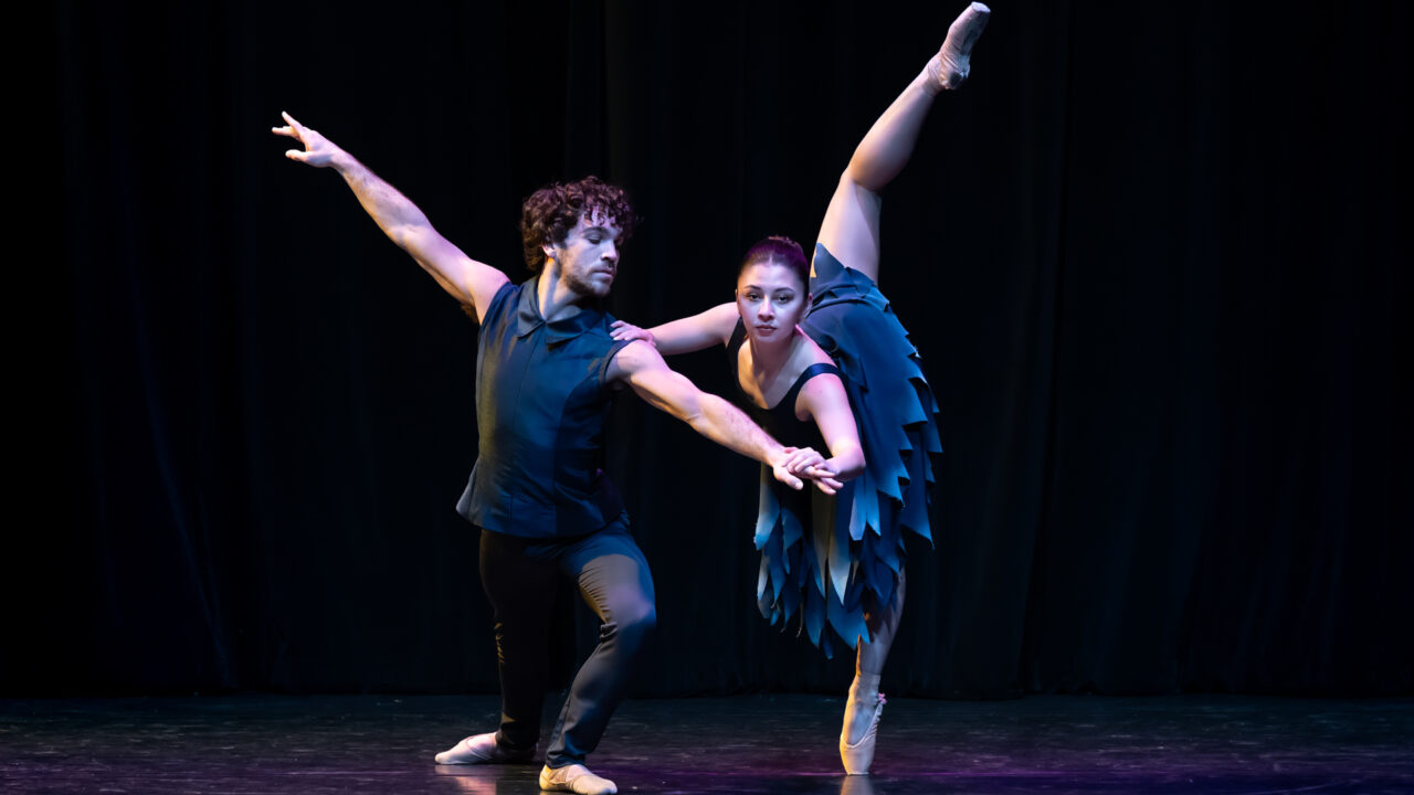 male dancer supports a female dancer who lifts her leg high in the air