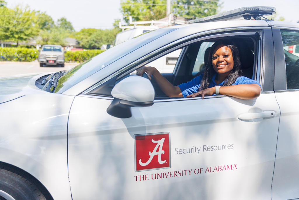 a UAPD security resource assistant driving a white car while smiling