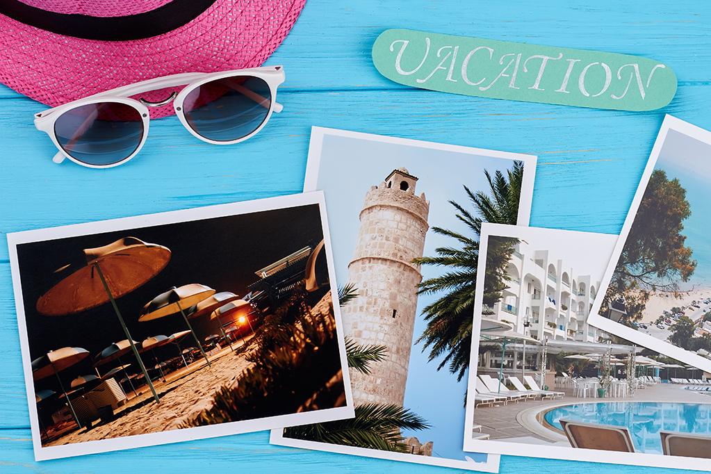 A hat, sunglasses and photos of vacation destinations with the word Vacation written on the photo.