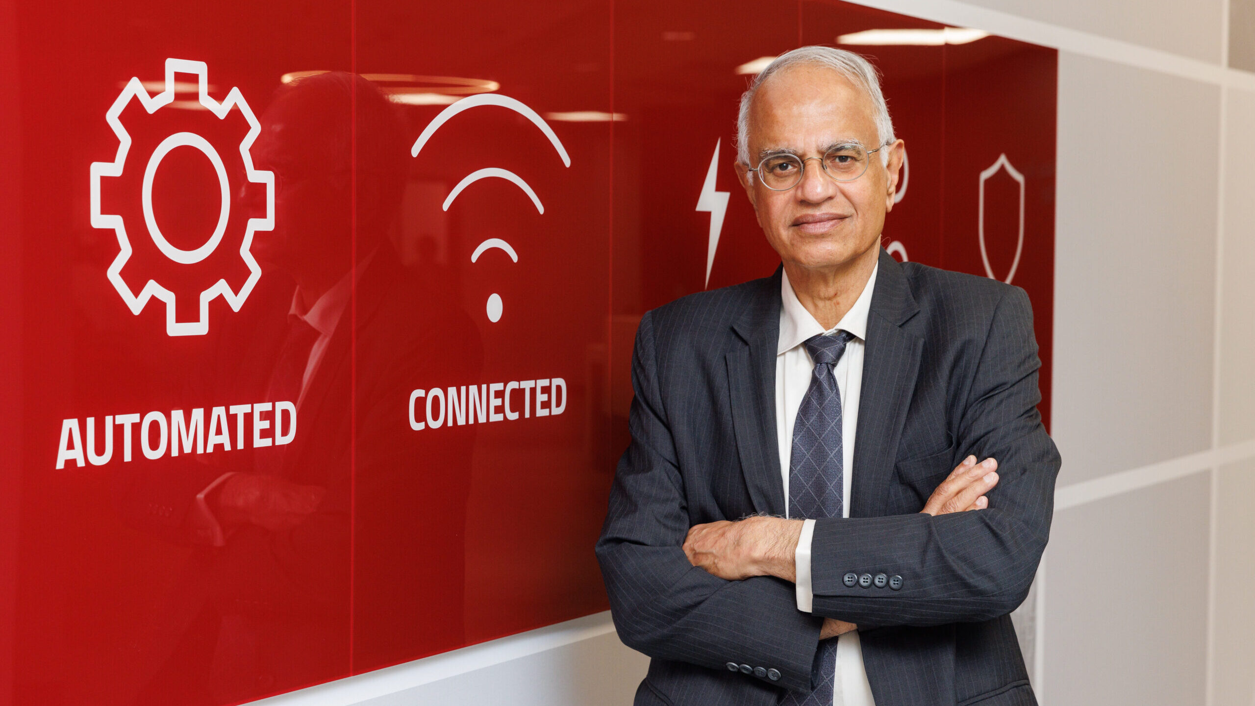 Dr. Bharat Balasubramanian stands in front of a sign with the words Automated, Connected, Shared and Safe.