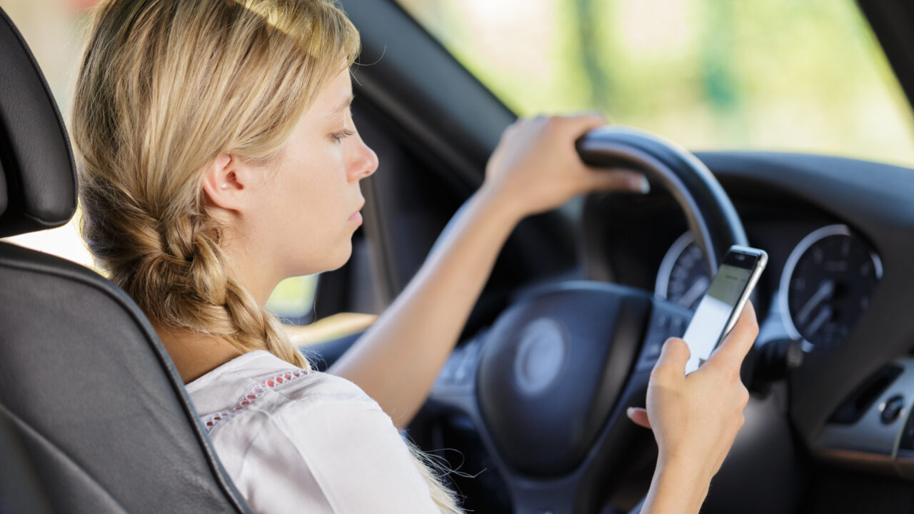 A person holding a mobile phone while driving.