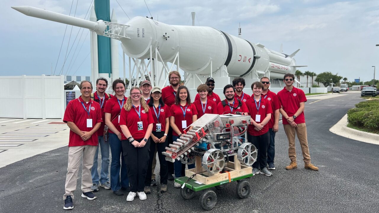 The University of Alabama Astrobotics team stands in front of a rocket with their winning lunar mining rover