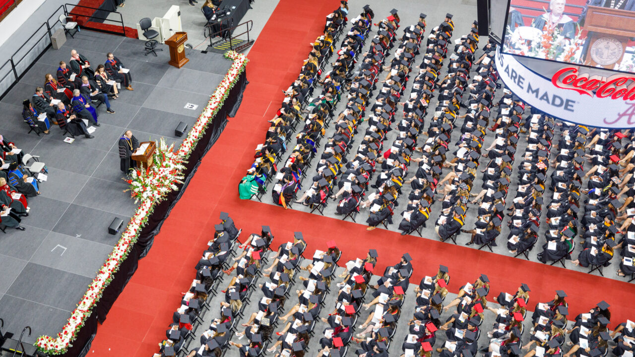 a bird's eye view of the commencement arena, showing the rows of graduates seated facing the stage