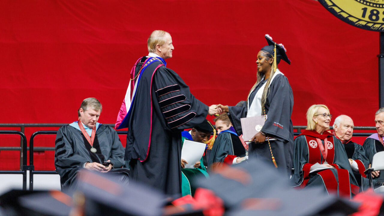 a young woman shakes Dr. Bell's hand on the commencement stage