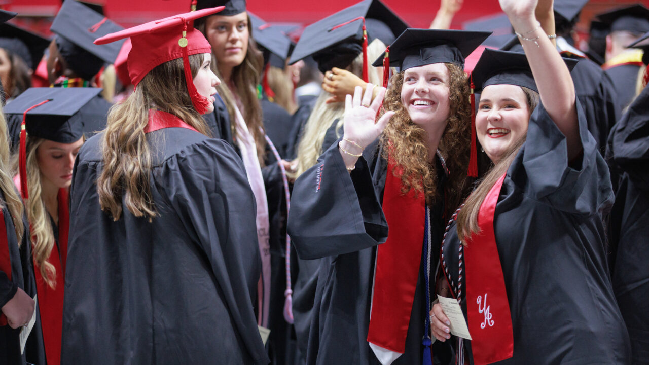 two graduates wave toward the crowd