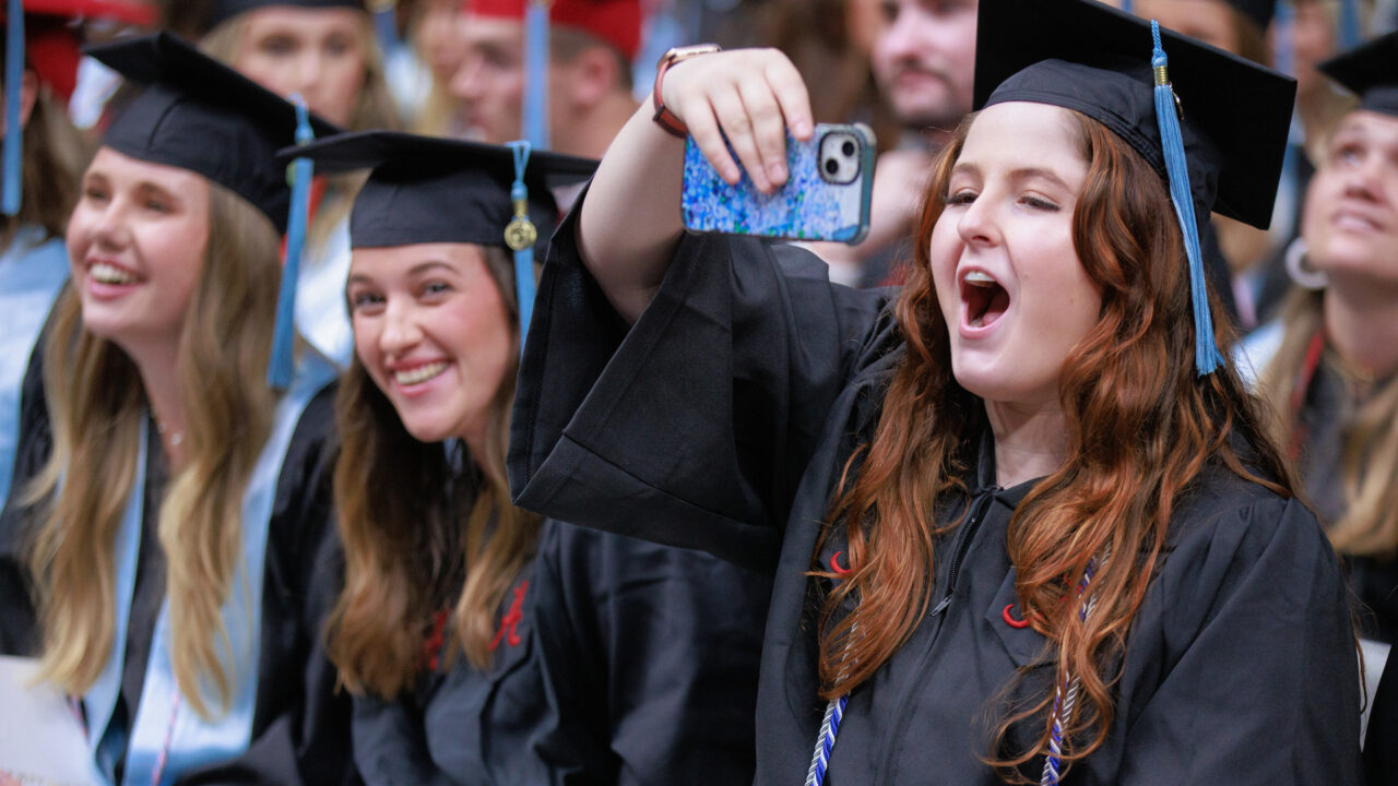 a young women graduate holds up her phone to take a picture