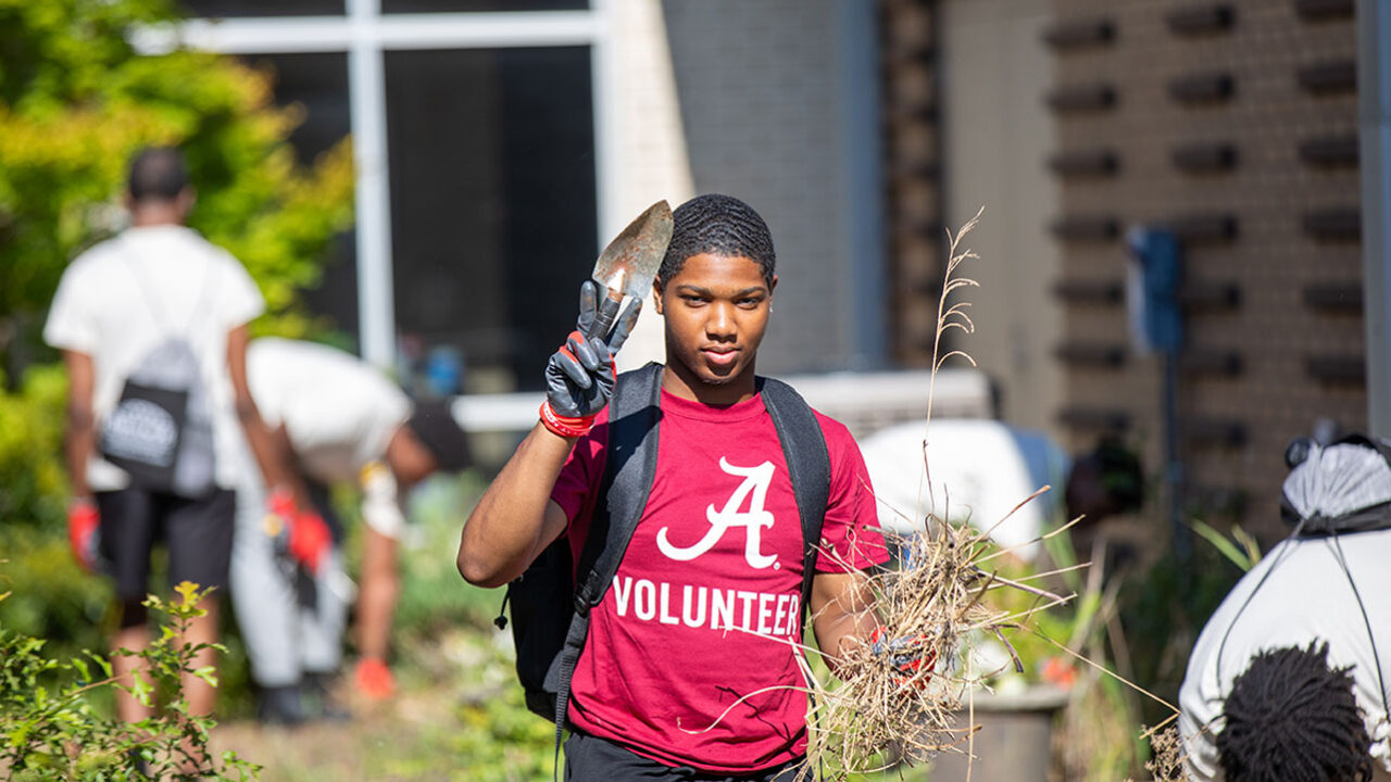 Black student holds a small shovel during volunteer landscaping work.