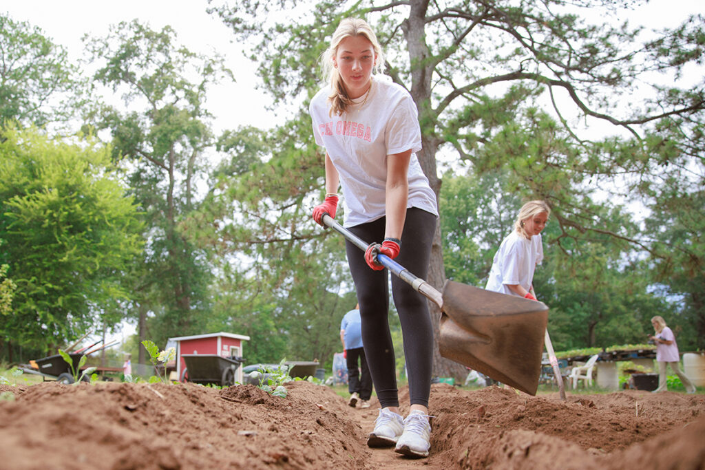 Three white female students volunteer doing landscape work.