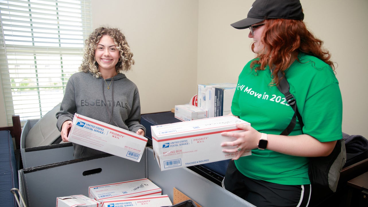 Two students unload U.S.P.S packages in a dorm room